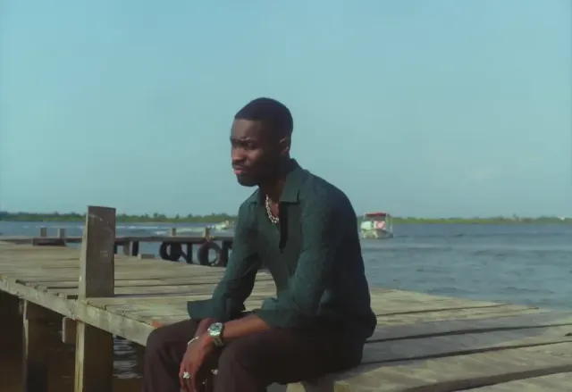 Performer seated on a wooden dock beside the water